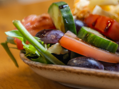 Image of a side salad, cucumber, tomato, lettuce, grapes with drizzle on a plate